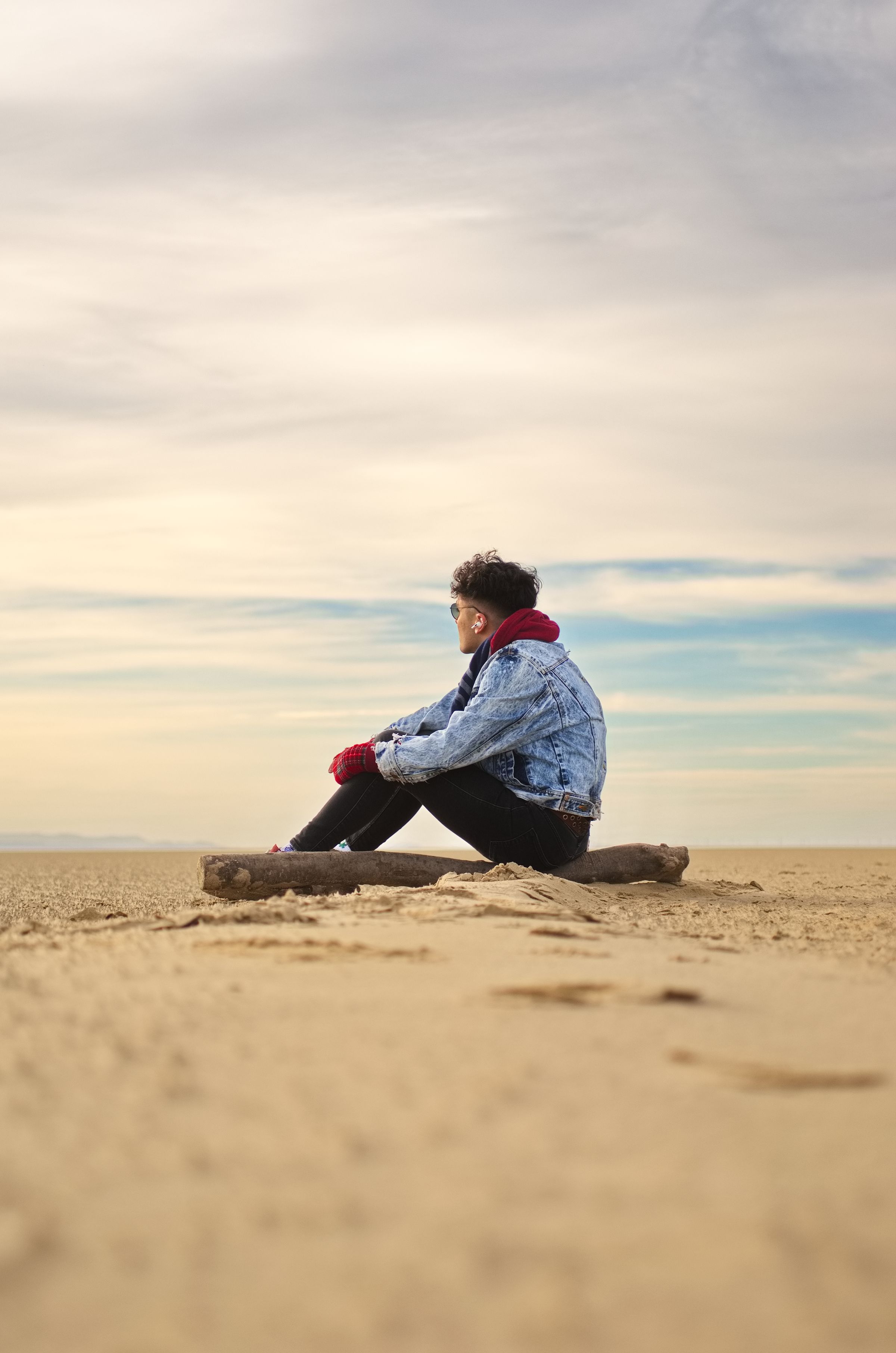 A man sat on a rock on the beach, looking into the distance.