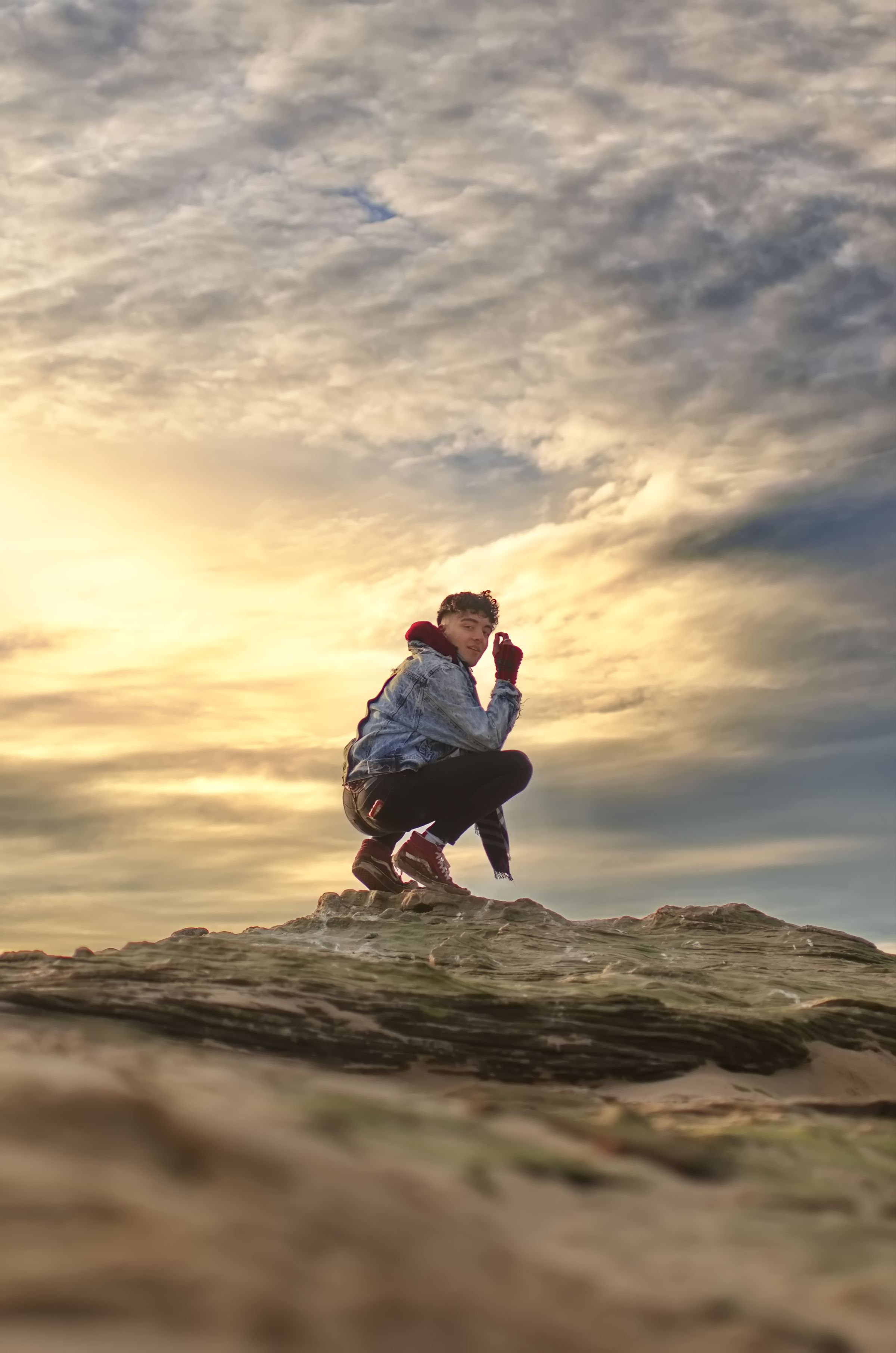 A man sat on top of a rock on the beach at sunset.