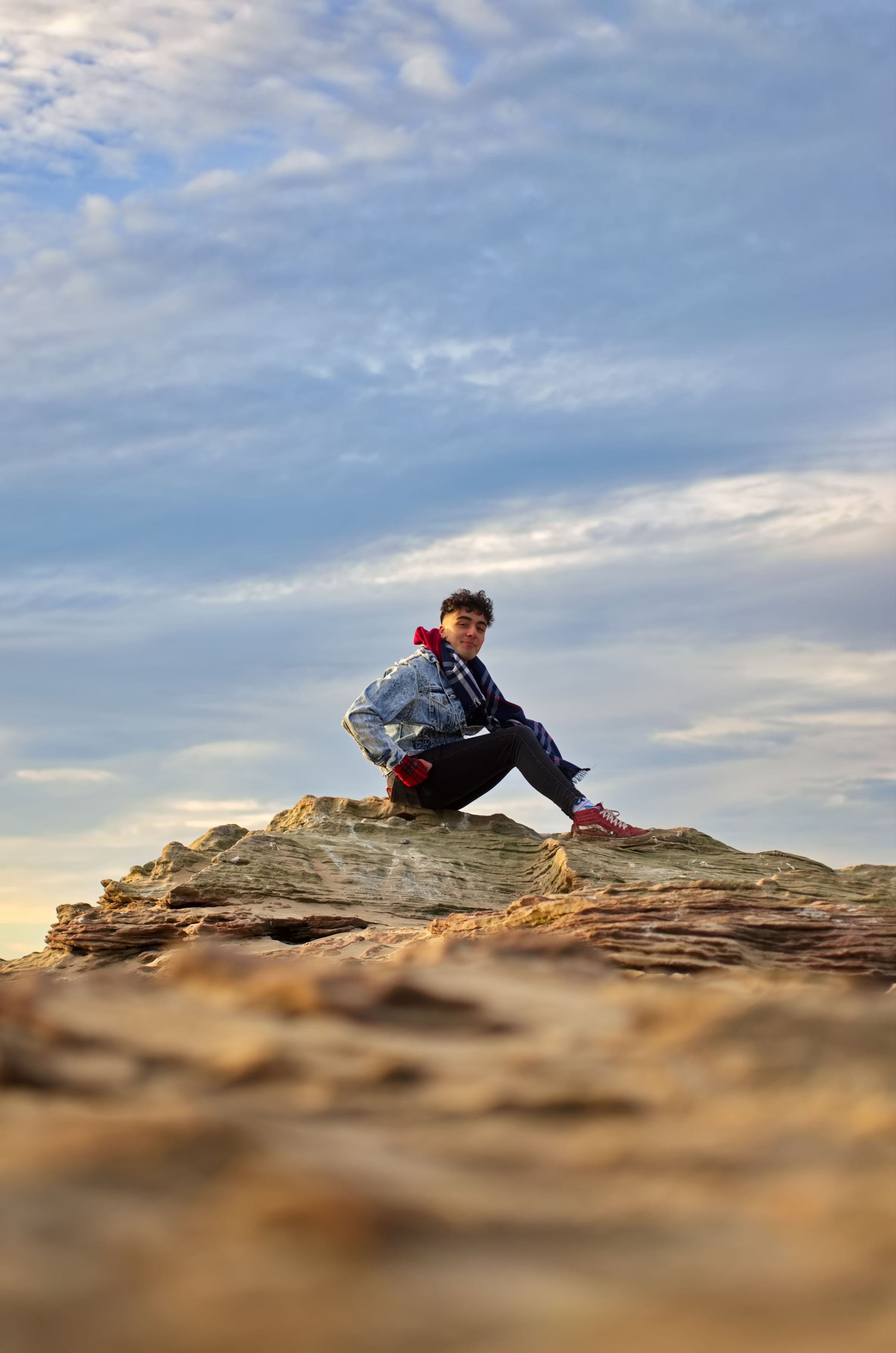 A man sat on raised rocks on the beach, in the sun.