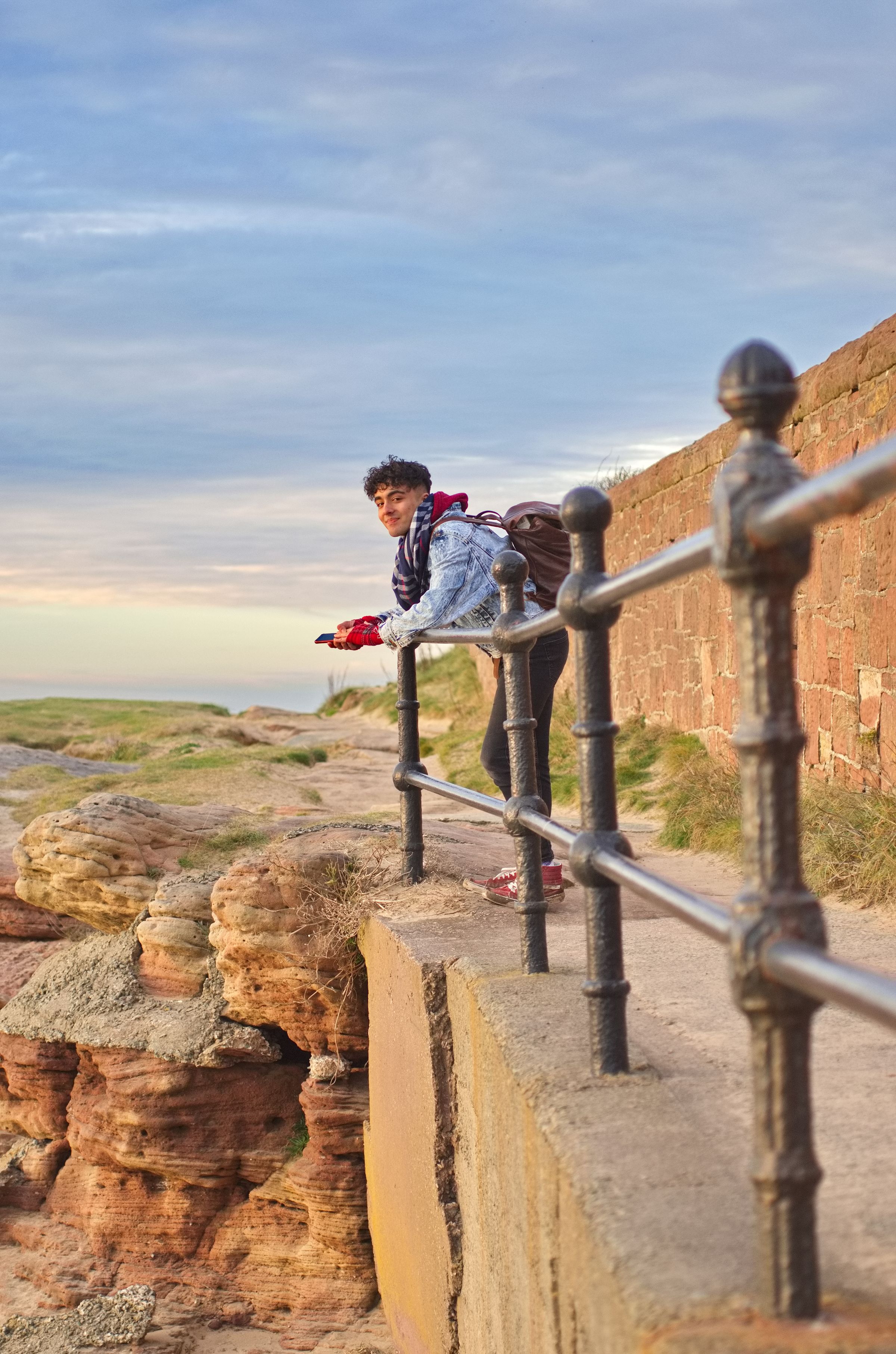 A man stood by a metal fence on the beach, looking at the ocean.