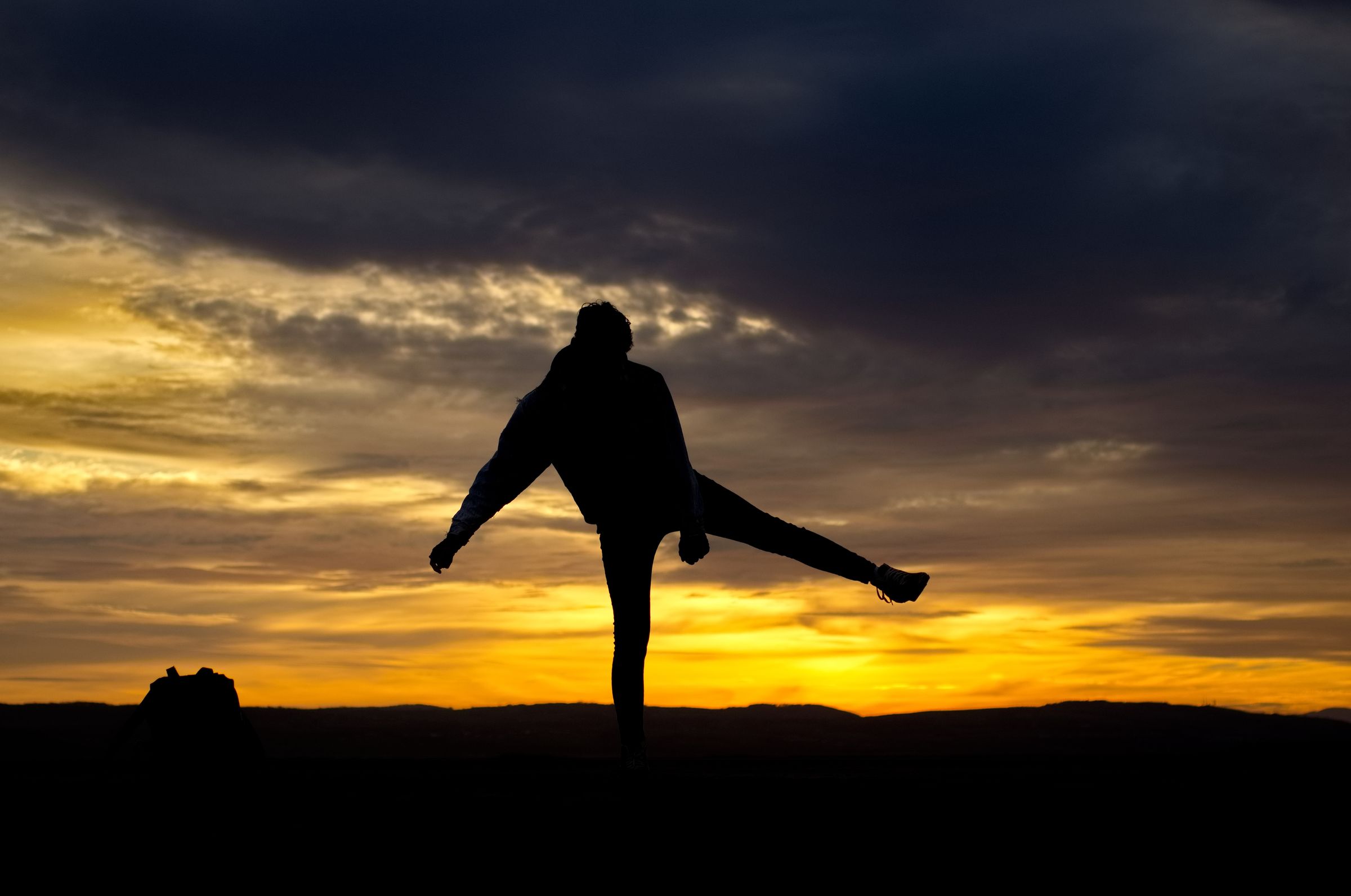 A silhouette of a person dancing on the beach at sunset.