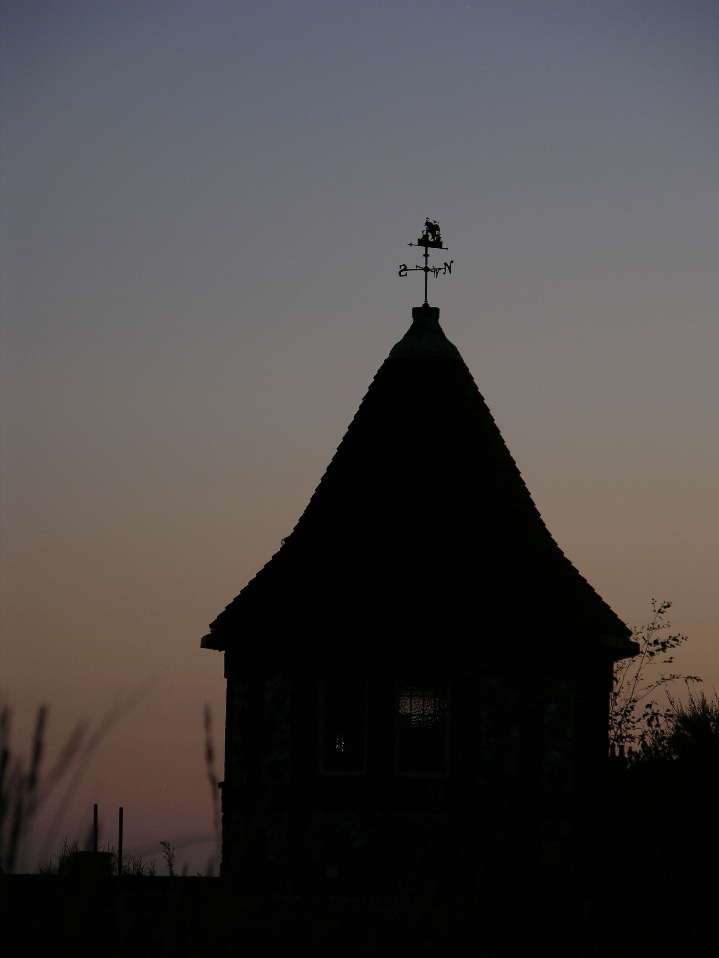 A silhouette of a hut with a pointed roof in a field at sunset.