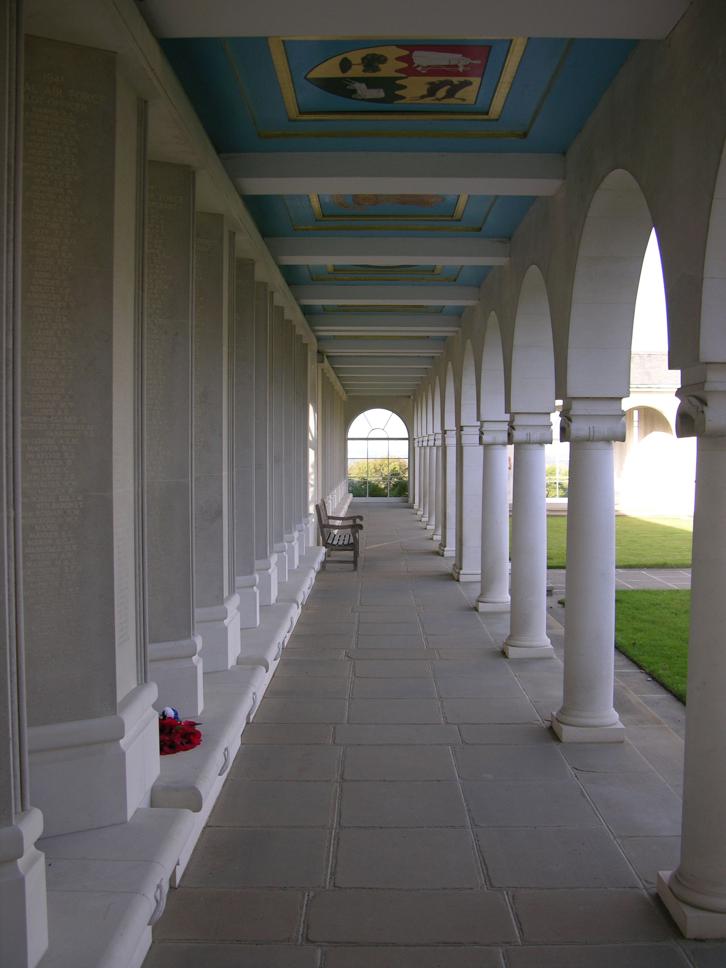 A straight coridoor in an air forces memorial with boards listing fallen soldiers, leading to a view over a forest through a window.