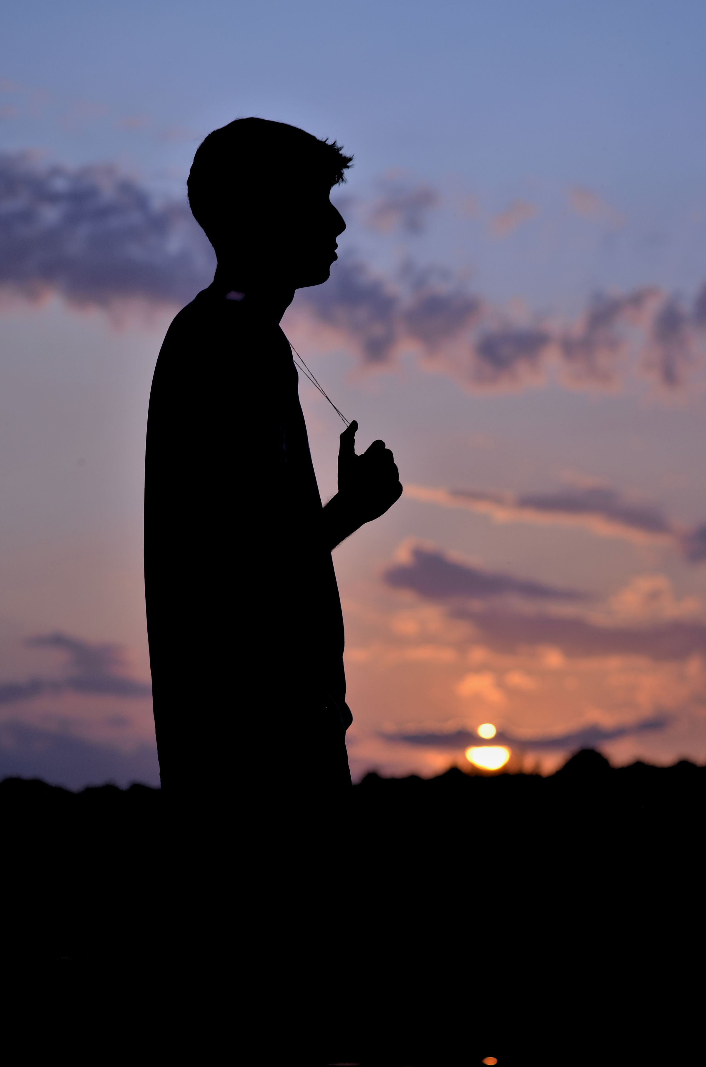 The silhouette of a man in the sunset, holding a necklace around his neck.